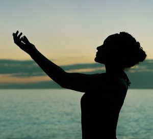 Silhouette of a woman standing sideways and lifting her hands and arms