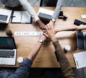 Birds eye view of desk with four workers hands meeting in the middle in union