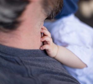 Close up photo of man's neck with babiy's hand holding onto him